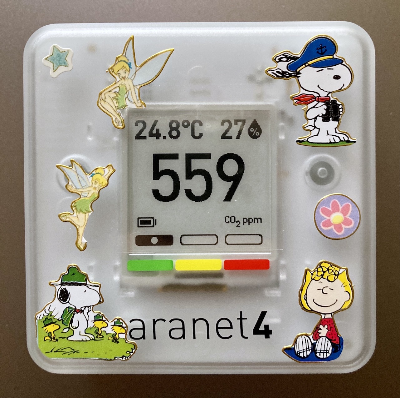 The front side of an Aranet4 device. The space surrounding the screen has been decorated with various small stickers depicting Tinkerbell and characters from Peanuts.